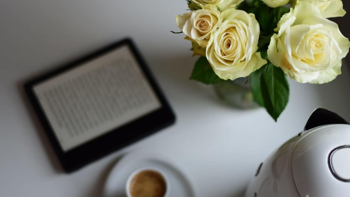Elegant white roses, coffee, and e-reader create a serene morning setup.