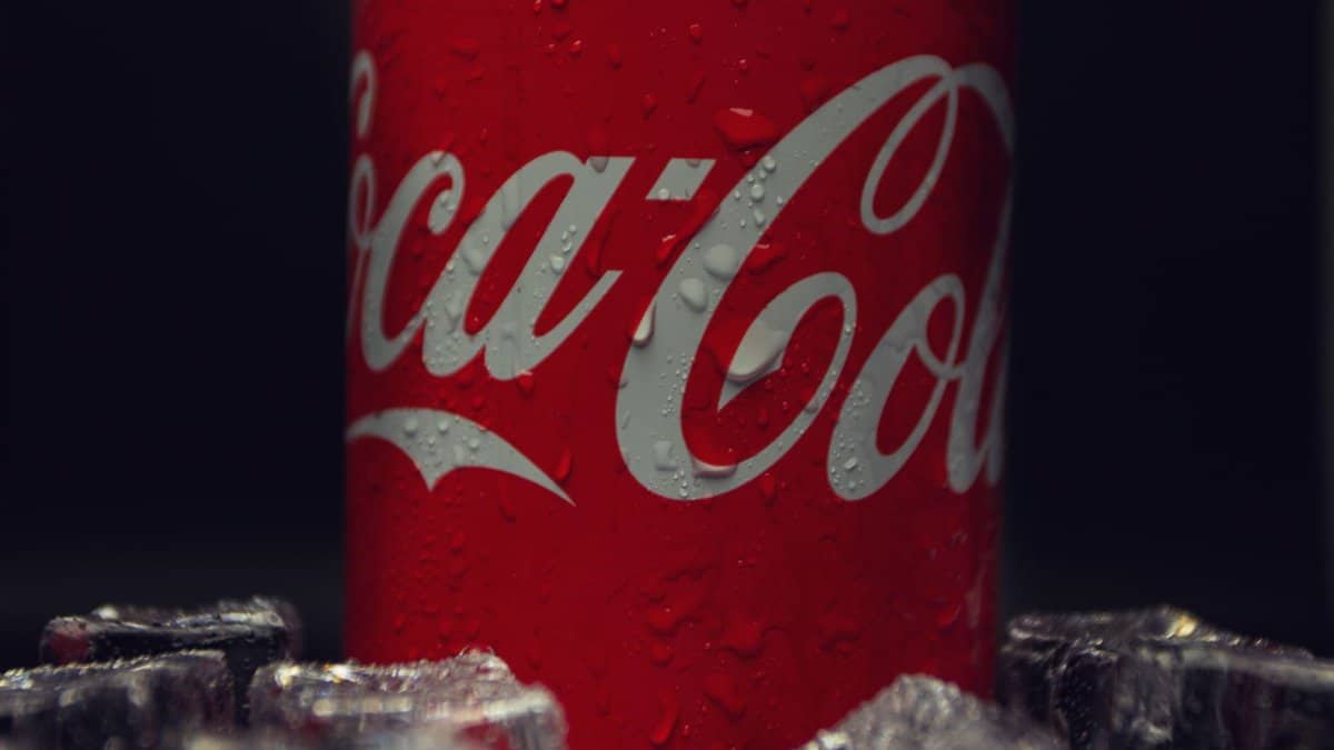 Close-up photo of a Coca-Cola can with dew droplets and ice cubes, refreshing concept.