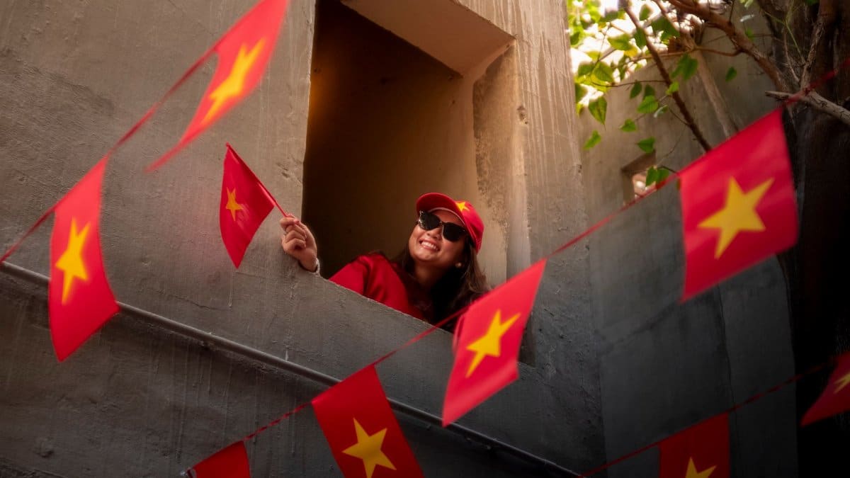 A woman joyfully waves a Vietnamese flag amidst red banners in an urban setting.