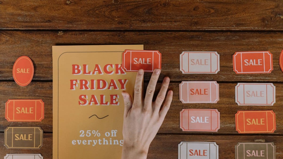 Top view of hand arranging Black Friday sale flyers on wooden table, offering 25% off everything.