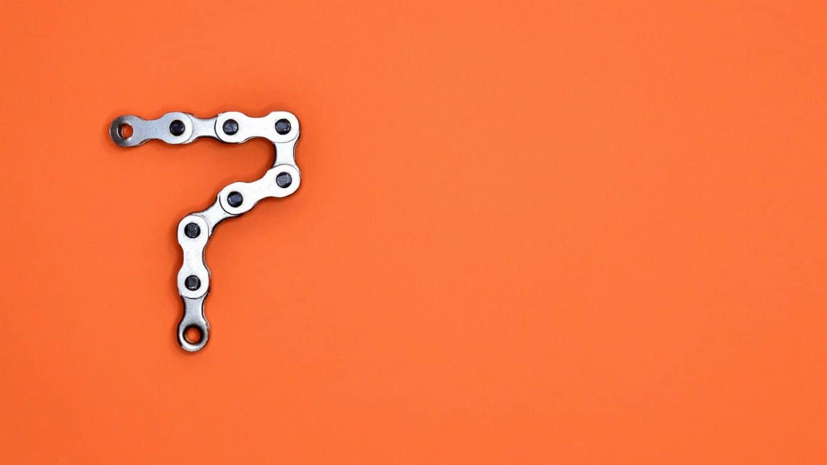Artistic arrangement of bicycle chain shaped like number seven on orange background.
