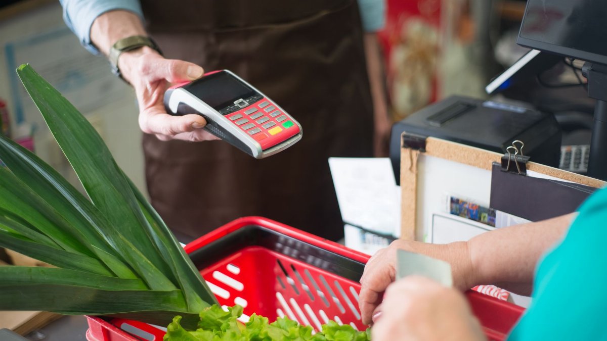 A customer using a contactless payment method at a grocery store checkout with fresh produce.