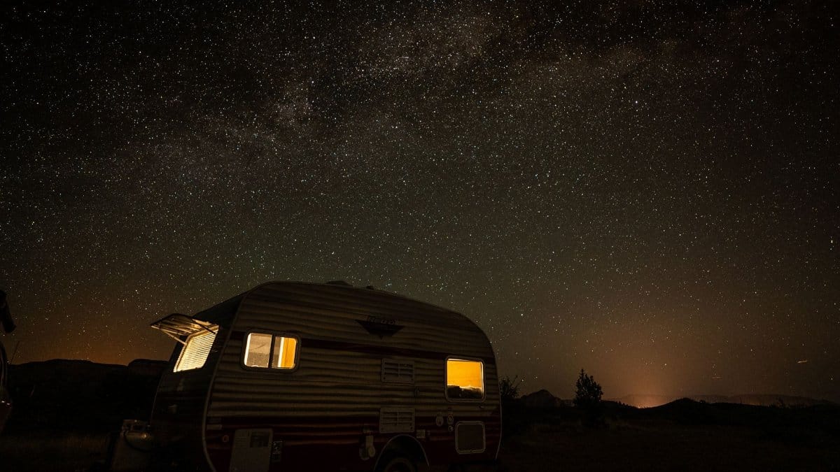 An illuminated vintage camper under a breathtaking starry night sky, showcasing the Milky Way.