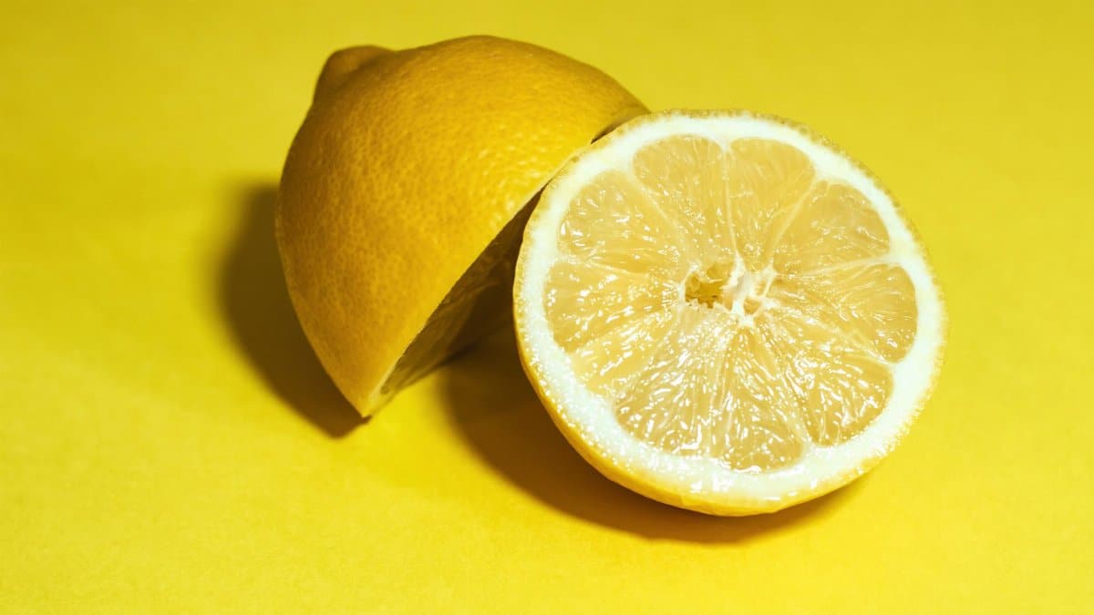 Close-up of a juicy lemon sliced in half, set against a vivid yellow background.