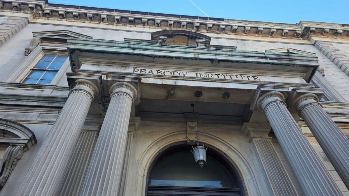 Low angle view of Peabody Institute entrance with classic columns against a clear blue sky.