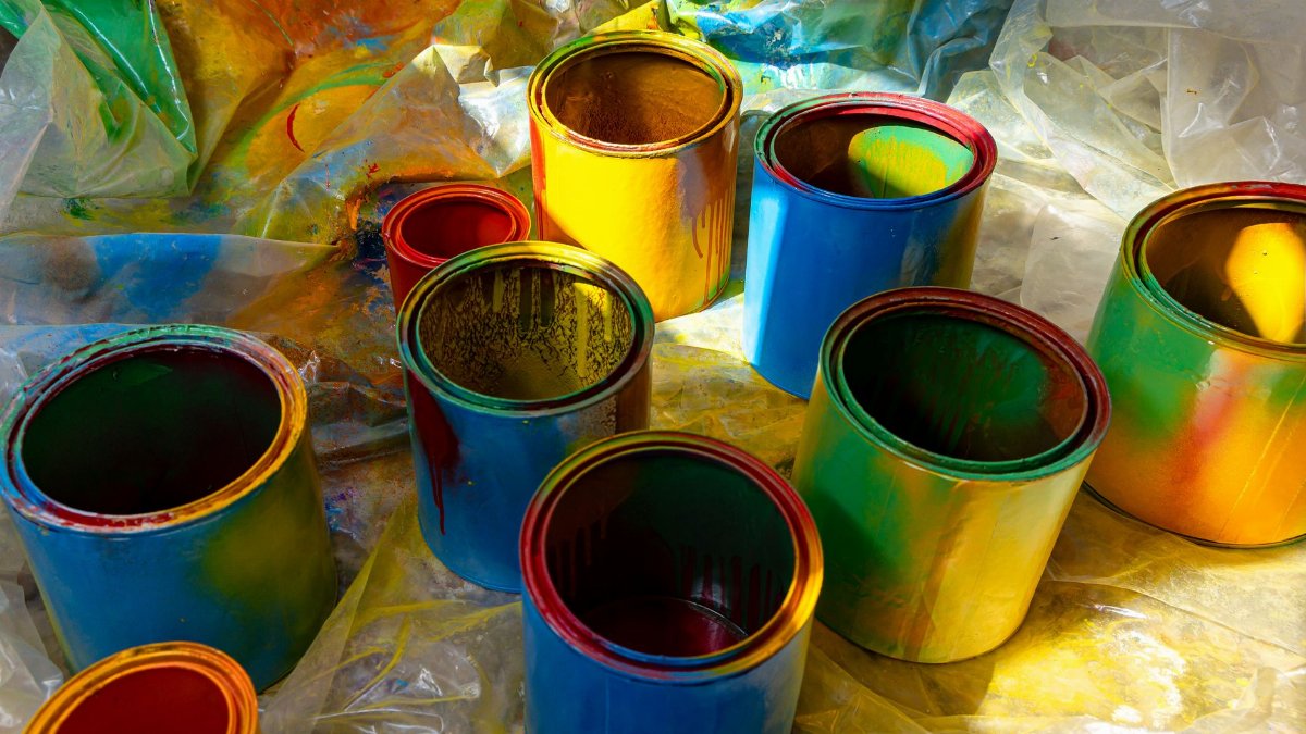 Colorful open paint cans on a plastic sheet with vibrant colors spilling over. Perfect for art and DIY themes.