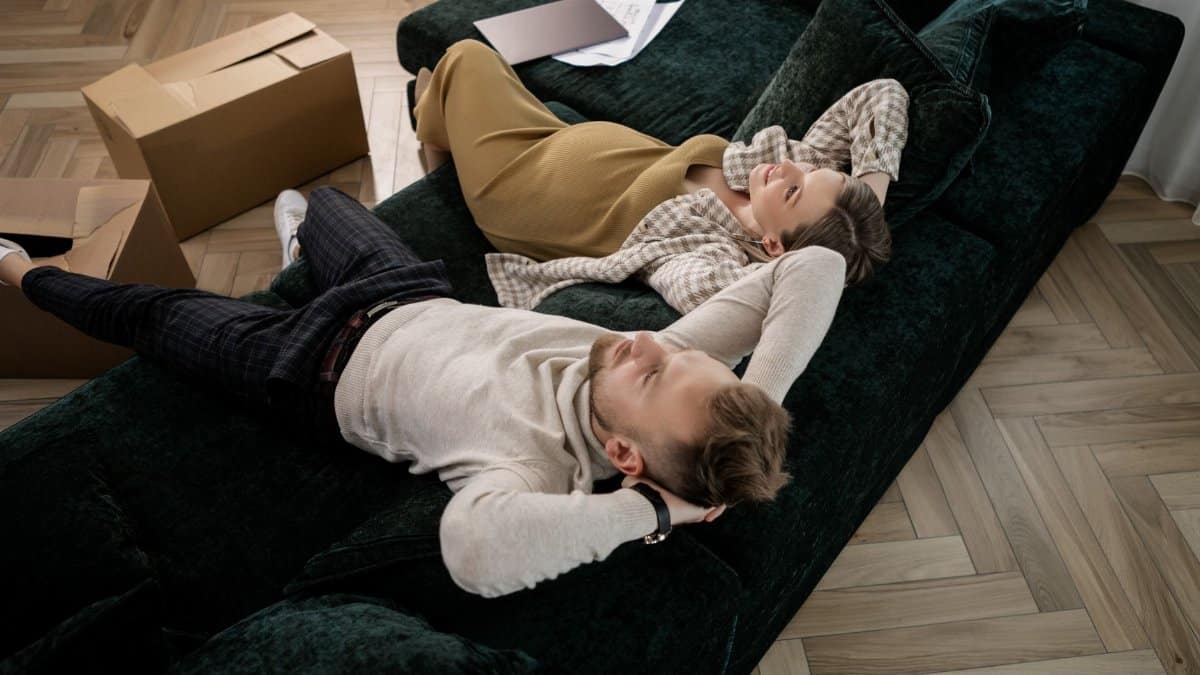 Expectant couple relaxing on a green sofa amidst moving boxes in their new home.