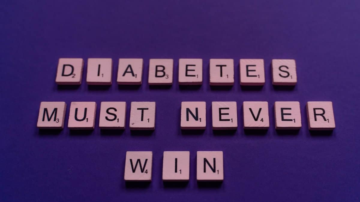 Scrabble tiles spelling 'Diabetes must never win' on a purple background for awareness.