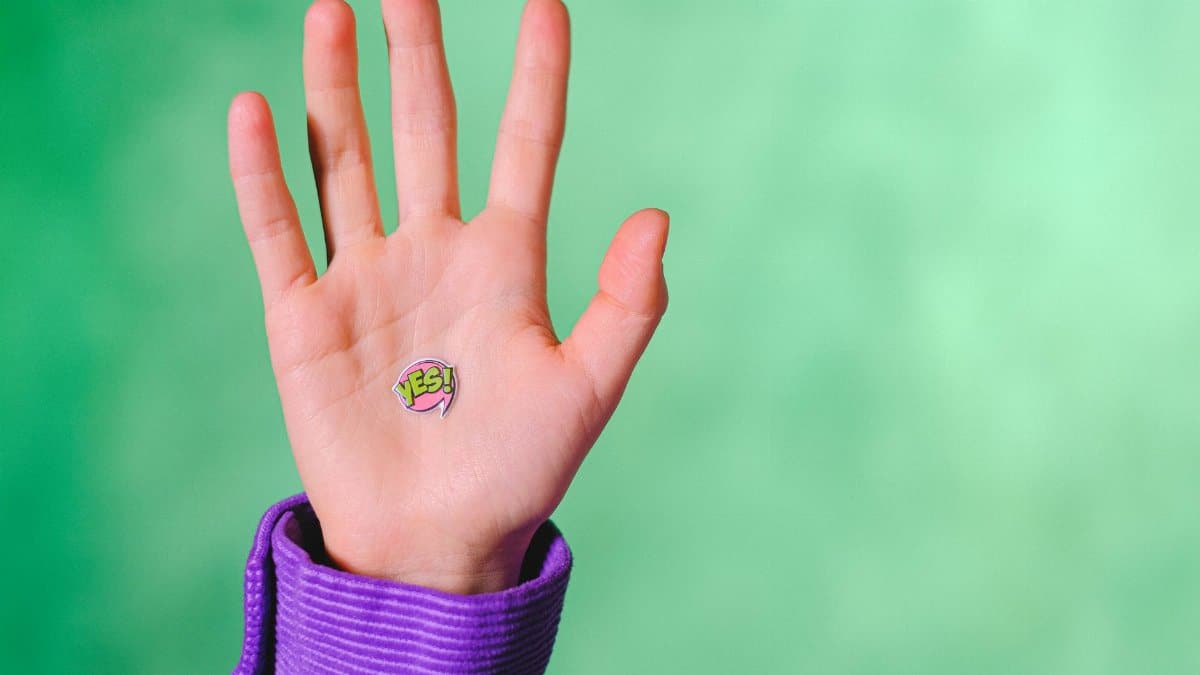 Crop anonymous person demonstrating sticker with word Yes placed on hand against green background