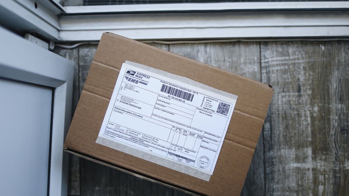 Brown cardboard box with shipping label on wooden floor near door, ready for delivery.
