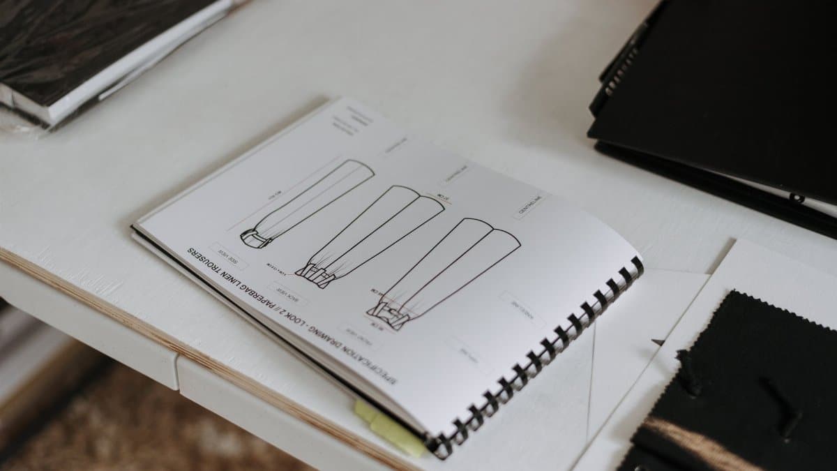 From above of sketchbook with sketches of new collection of clothes placed on white table in modern light professional studio with various folders