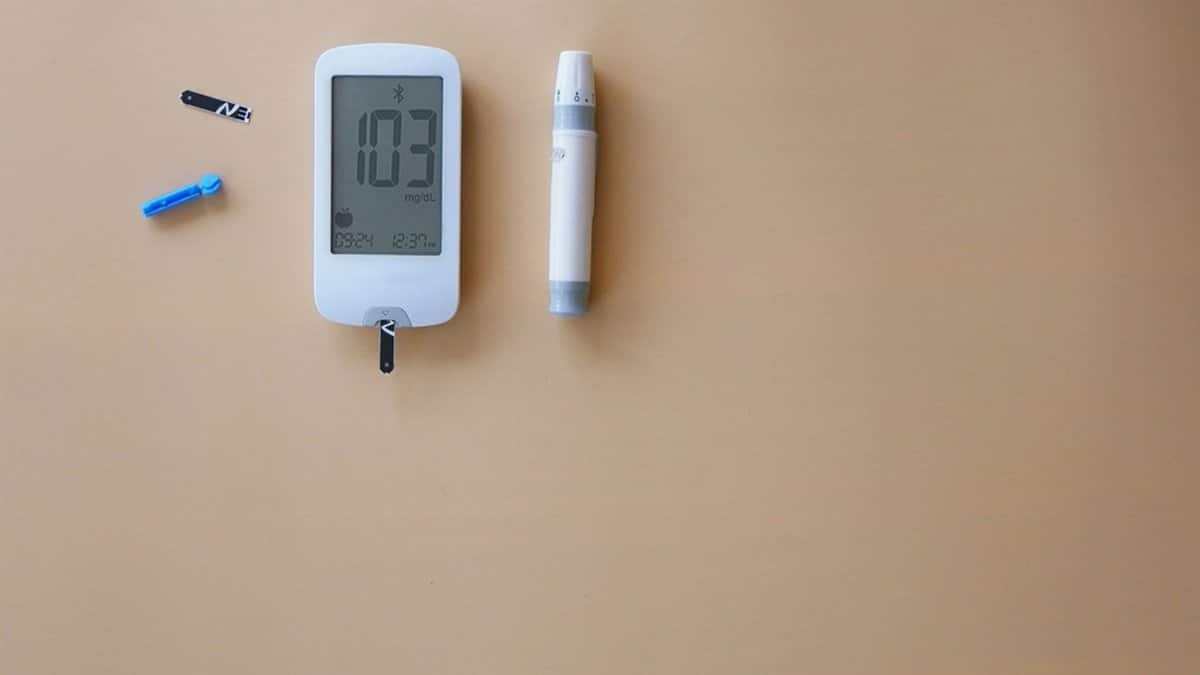 Blood glucose meter, test strip, and lancet on beige background for diabetes monitoring.