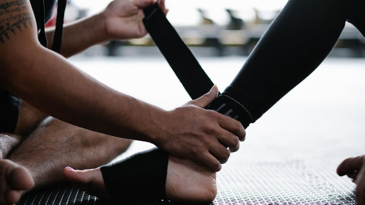 Close-up of an athlete's ankle being wrapped with an elastic bandage in a gym setting.