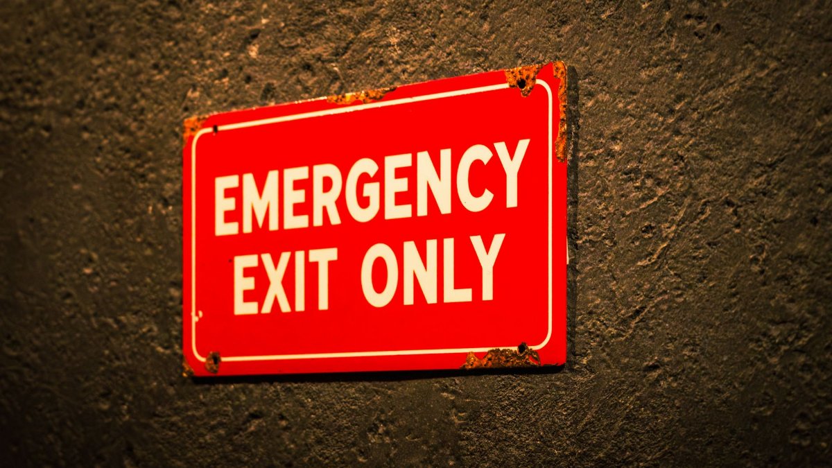 A vintage-style emergency exit sign on a textured wall, emphasizing safety and industrial themes.