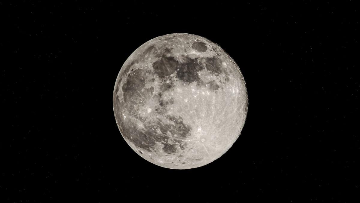 A detailed view of the full moon illuminating the night sky with stars in the background.