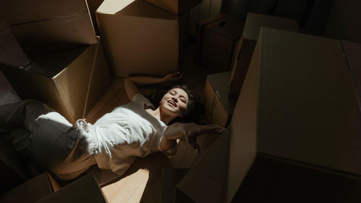Woman lying casually among moving boxes, experiencing a moment of rest and happiness.
