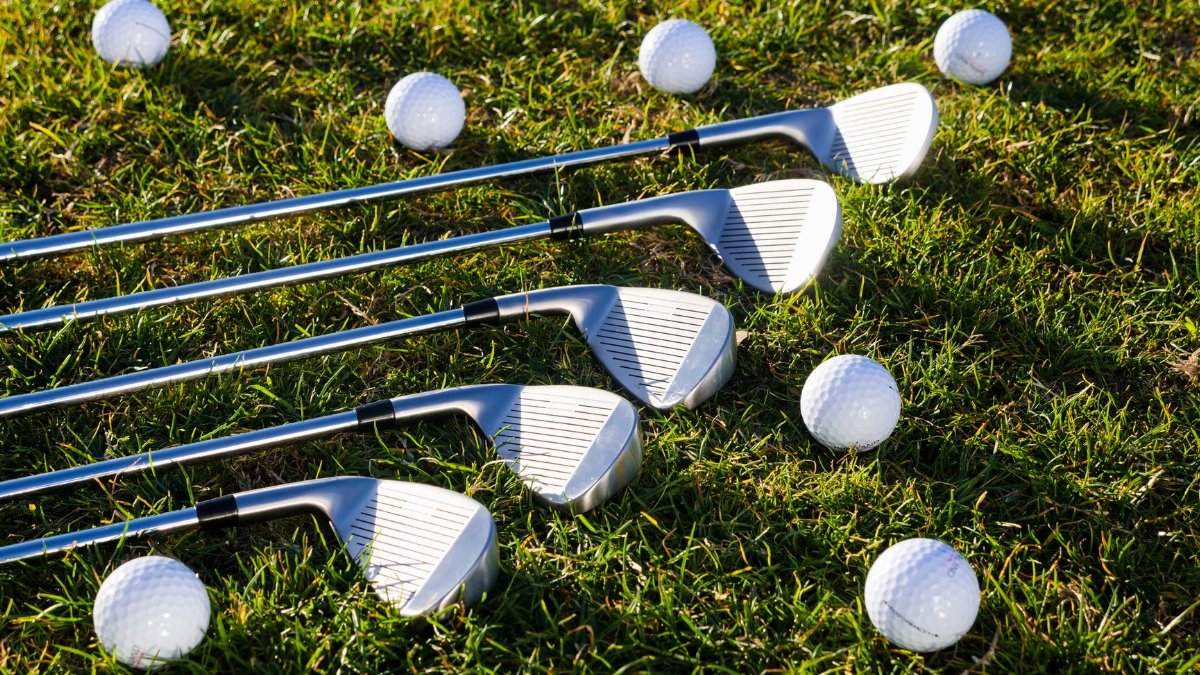 Close-up of golf clubs and balls scattered on green grass, perfect for sports equipment use.