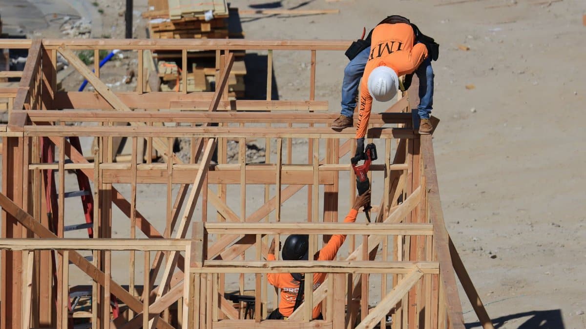 Two construction workers framing a wooden structure outdoors at a building site.