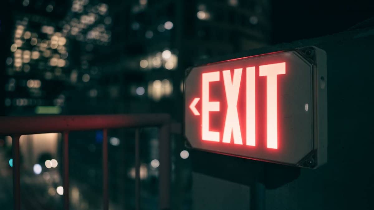 Bright red exit sign glowing against a blurred urban cityscape at night.