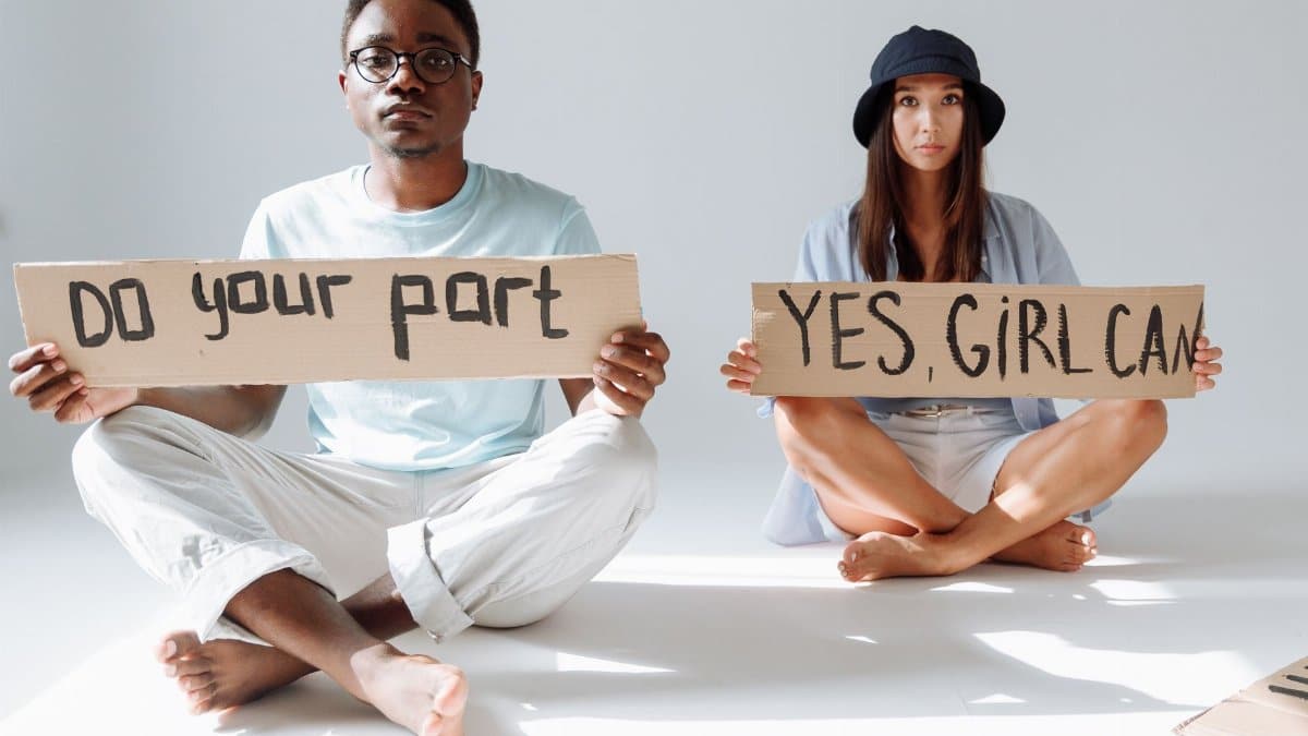 African American man and Asian woman sitting with cardboard signs promoting empowerment.