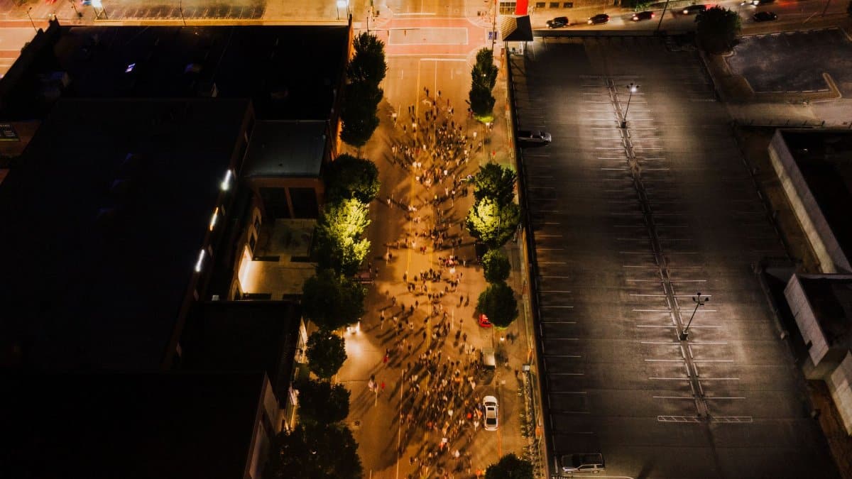Drone view of people going along blocked road in illuminated city at nighttime
