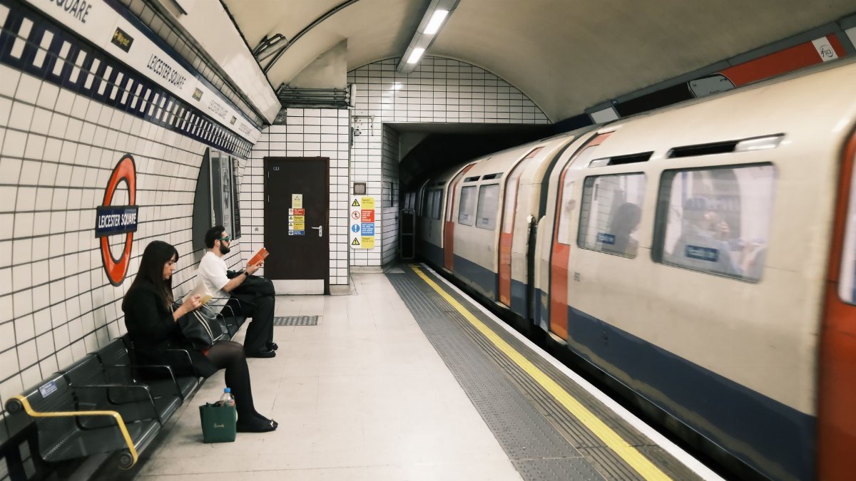 Commuters waiting at Leicester Square station with a train passing by.