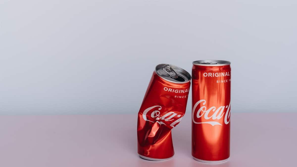Two Coca Cola cans, one crumpled, on a minimalist tabletop with ample copy space.