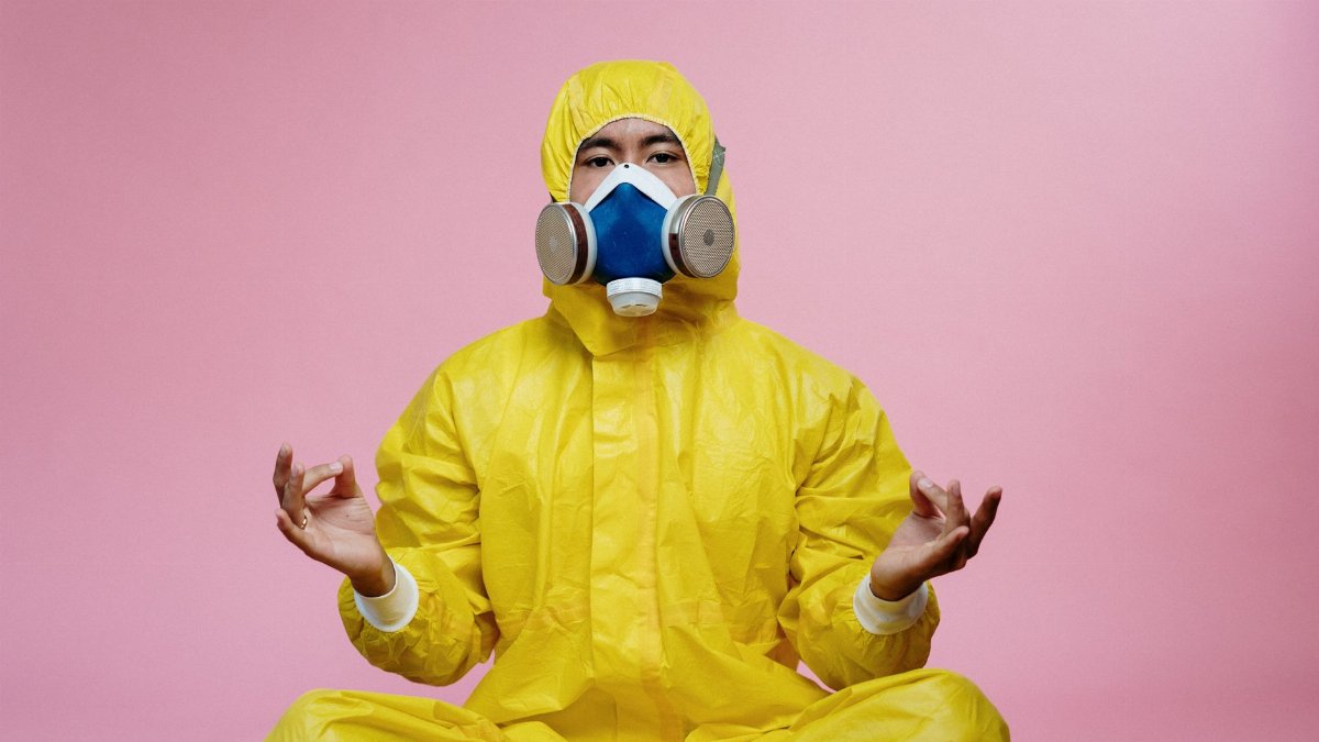 Person in a yellow protective suit meditating against a pink background.