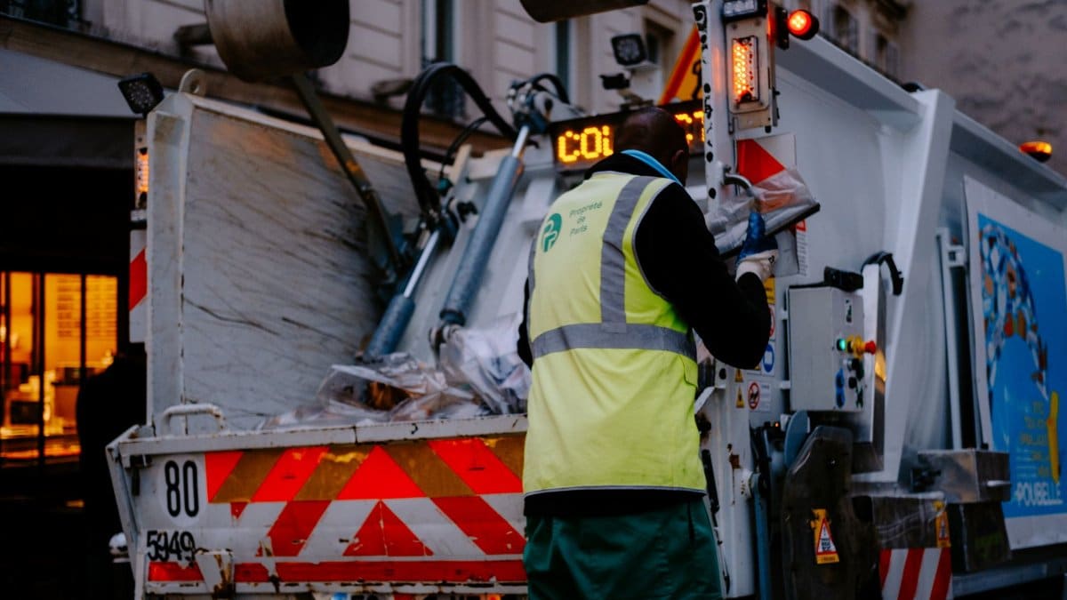 A garbage collector works on a city street, managing waste collection at dusk.