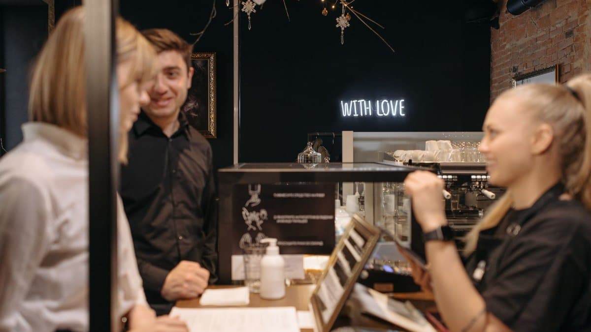 Customers engaging with a barista in a cozy coffee shop featuring warm lighting and decor.