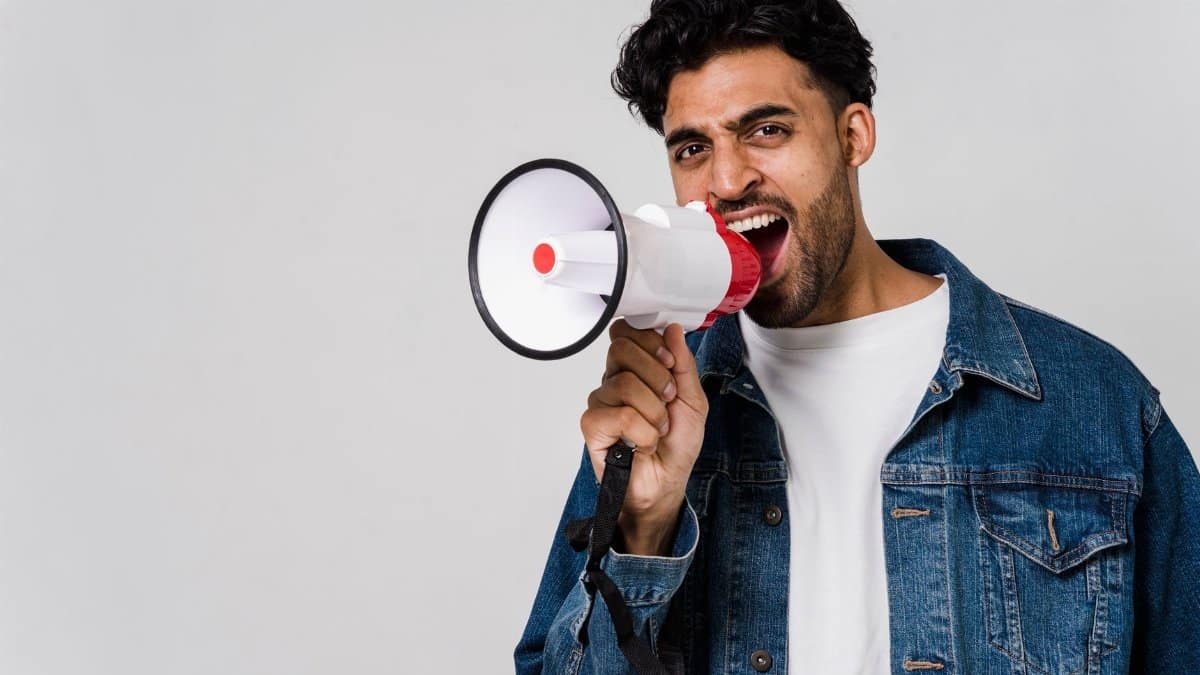 Energetic young man shouting into a megaphone, expressing enthusiasm in a studio setting.