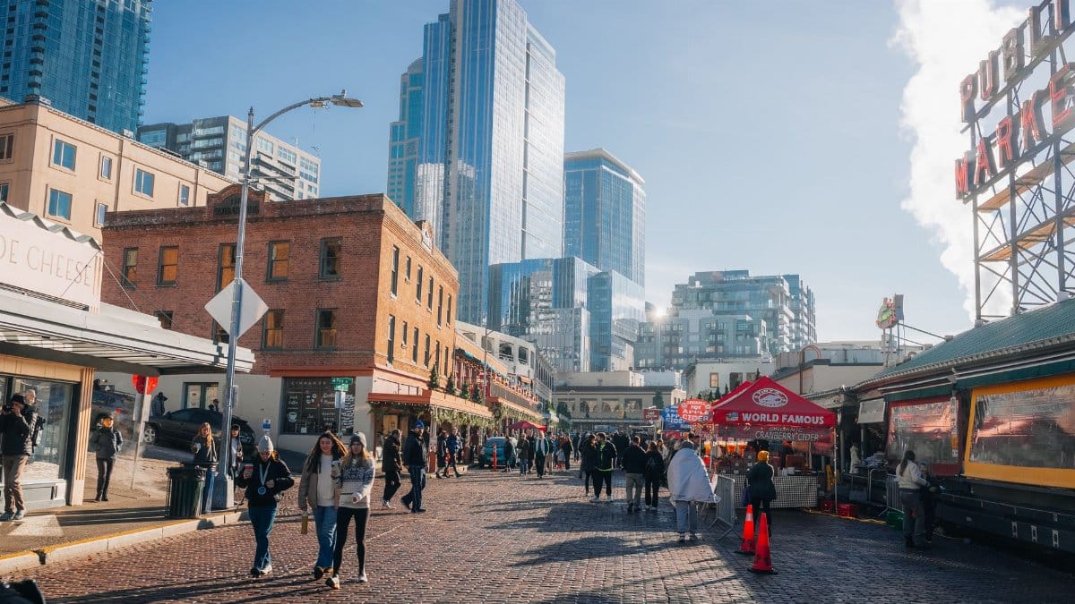 Bustling Pike Place Market in Seattle with iconic sign and skyline backdrop, capturing vibrant city life.