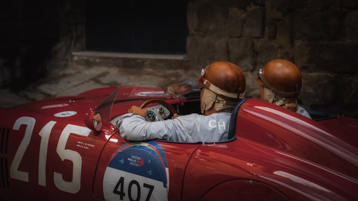 Two drivers in vintage helmets inside a classic red race car.