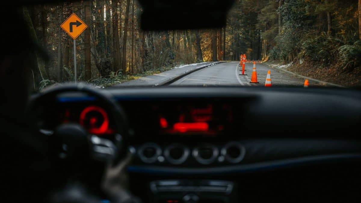 View from car dashboard of rural road with traffic cones and turn sign. Scenic forest driving experience.