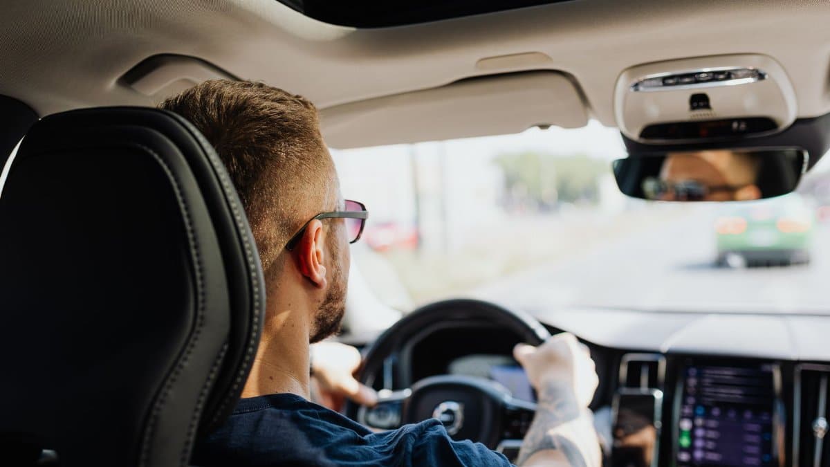Rear view of a man driving a car with focus on interior details and steering.