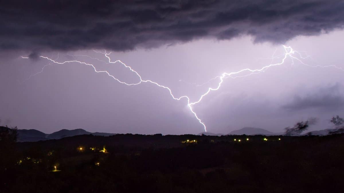 Dramatic nighttime capture of lightning striking over a rural landscape.
