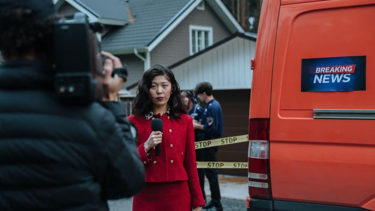 Female reporter in red with microphone reporting live at an outdoor crime scene with a news van.