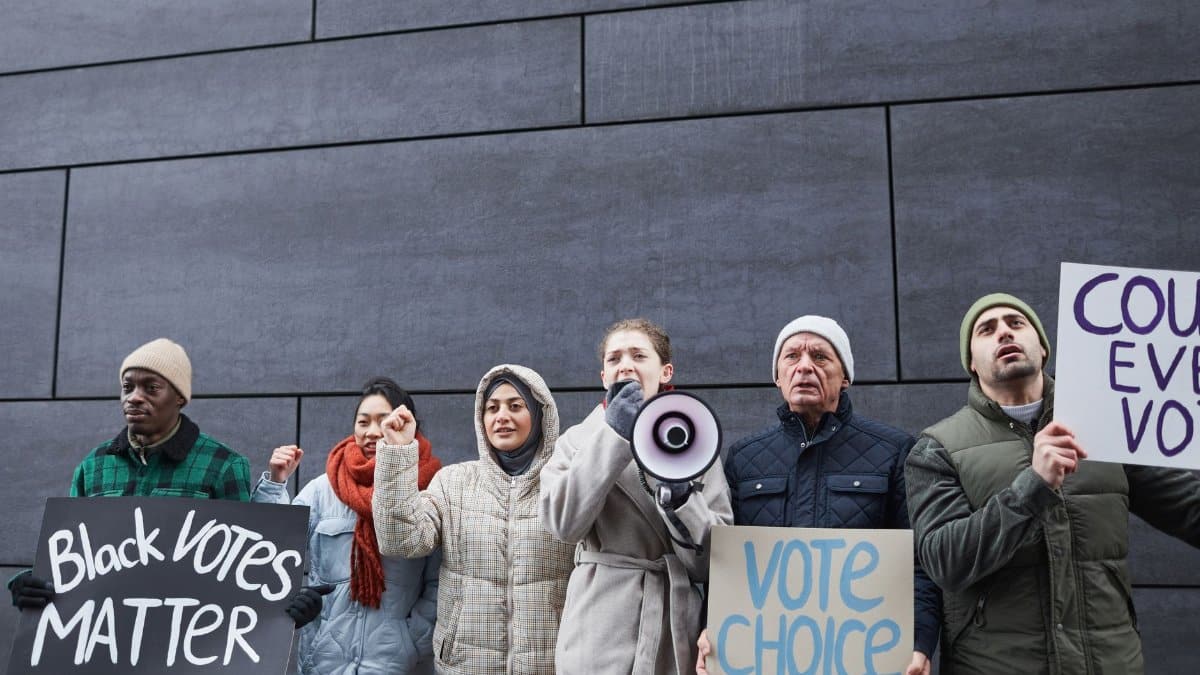 A diverse group of people protesting for voting rights, holding signs and a megaphone.