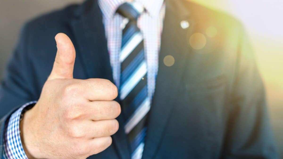 Close-up of a businessman in a suit giving a thumbs-up in a bright, positive setting.