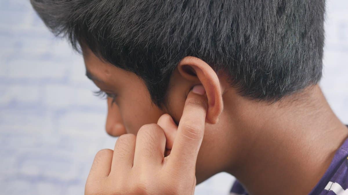 Close-up of a teenager's profile with hand covering ear, reflecting introspection or concentration.