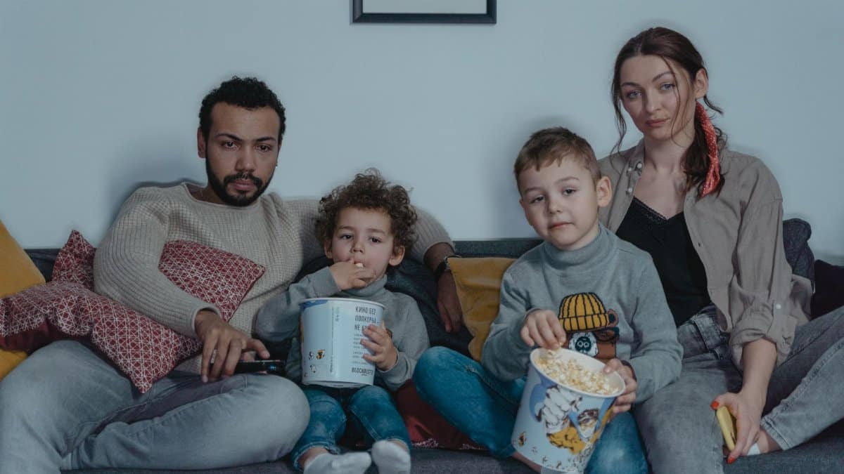 Family of four enjoying a cozy movie night with popcorn on the sofa.