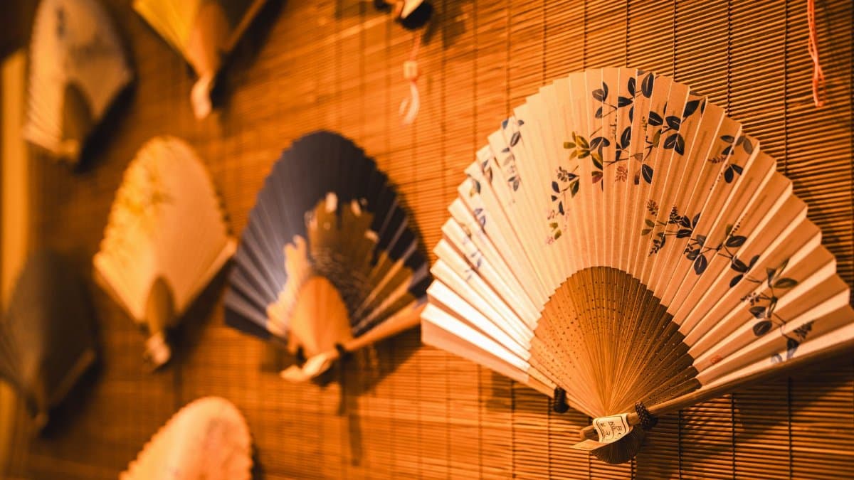 A display of traditional Japanese paper fans with intricate designs mounted on a bamboo wall.