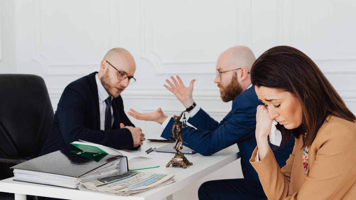 A woman appears distressed while two lawyers converse in an office.