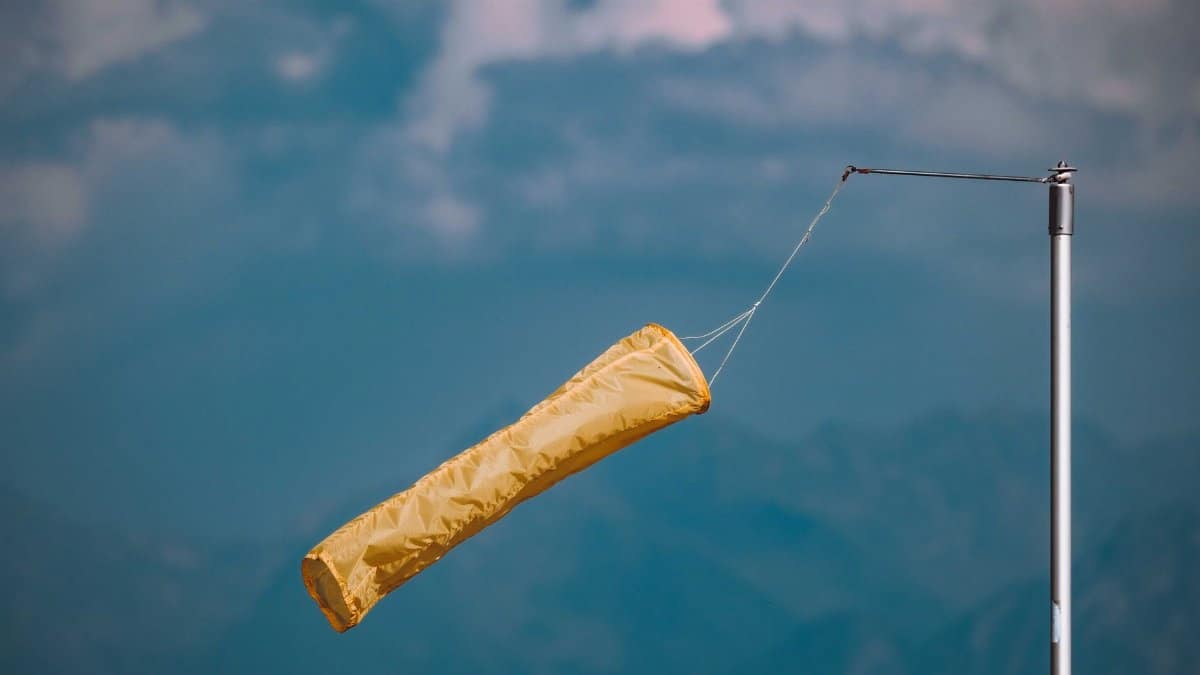 Yellow windsock blowing in the wind, mounted on a pole against a cloudy blue sky.