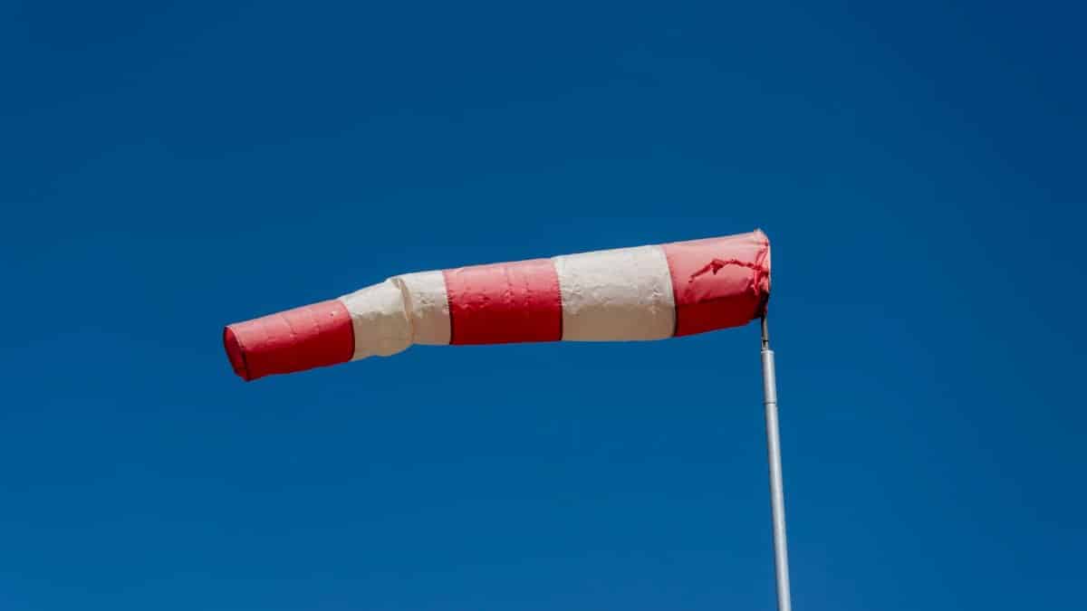 Vibrant red and white windsock blown by the wind against a clear blue sky.