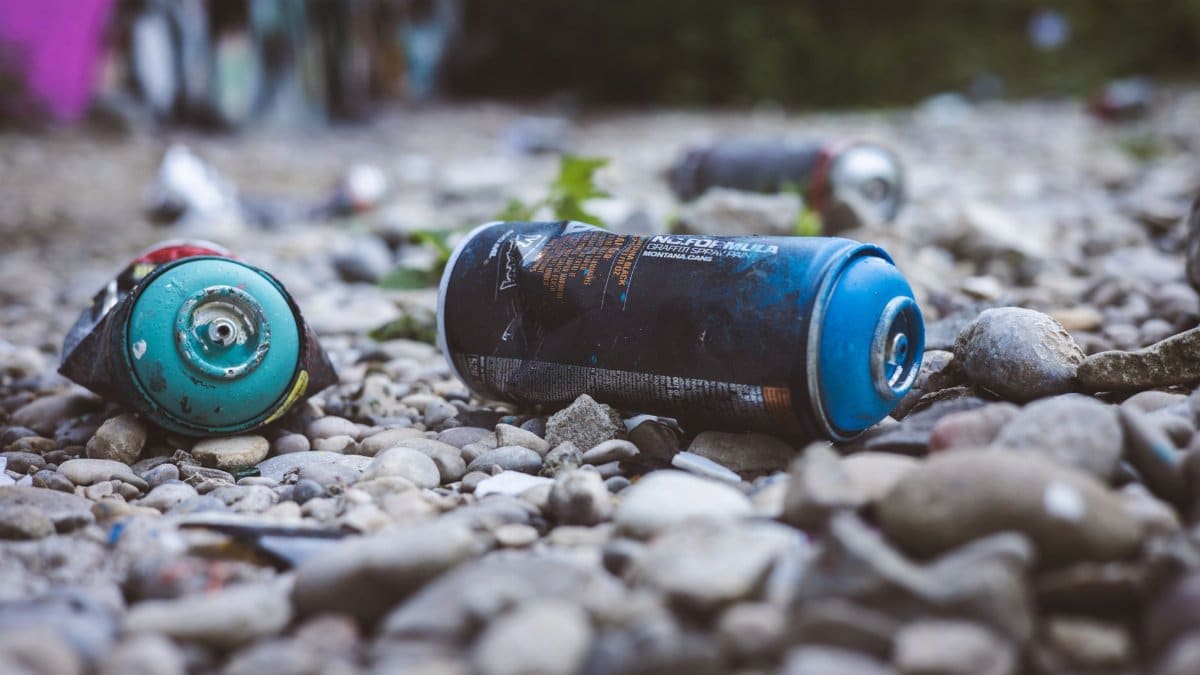 Close-up photo of discarded spray cans on rocky ground in outdoor setting, highlighting environmental waste.