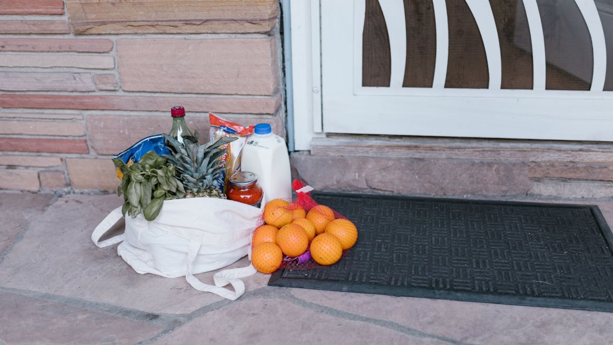 Reusable bag with groceries and fruits left at doorstep, highlighting delivery service.