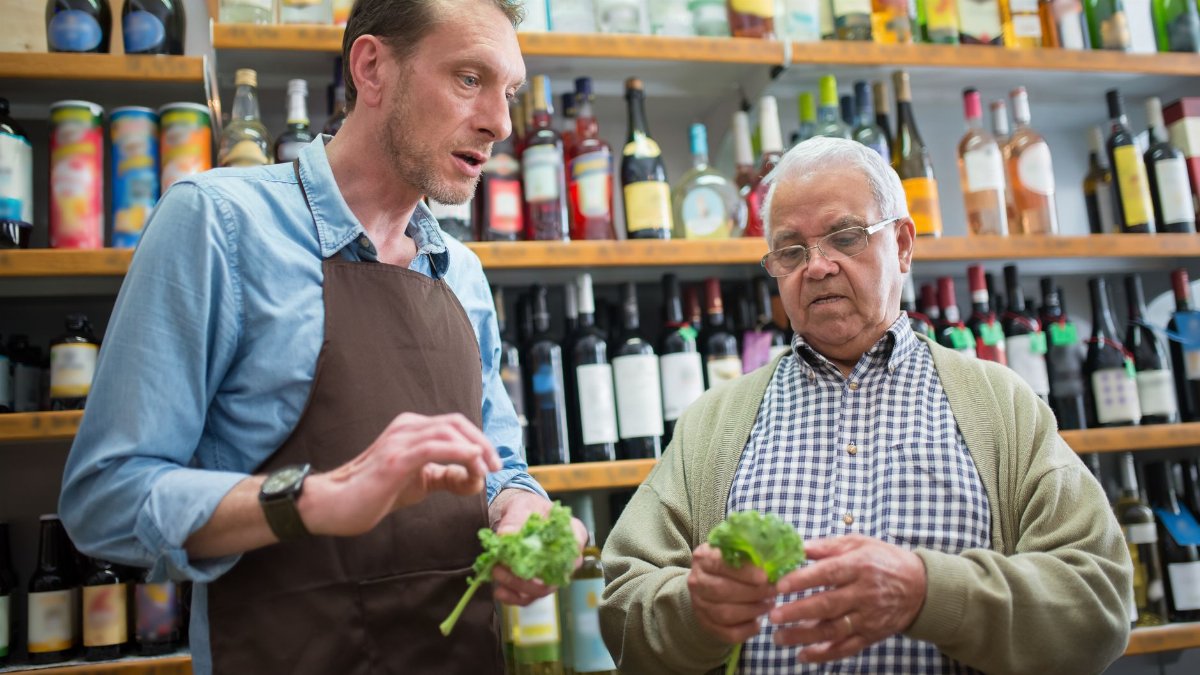 Senior man and store clerk examine fresh lettuce in a Portuguese grocery store.
