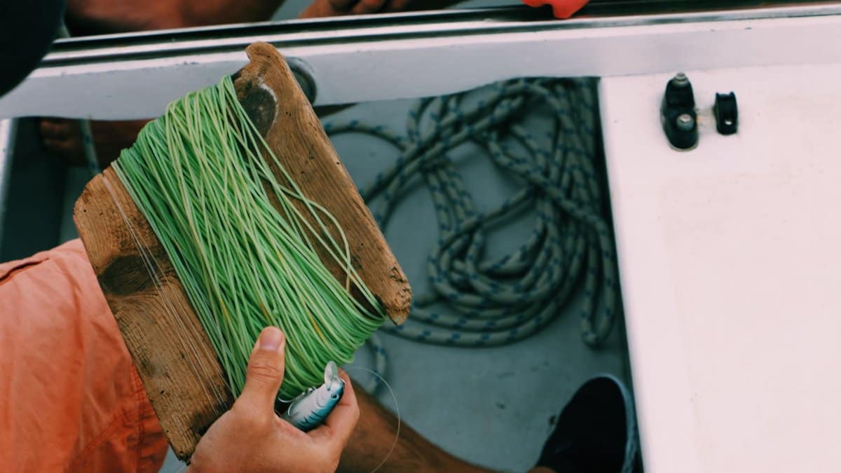 Person holding fishing line and tackle on a boat, showcasing preparation for fishing.