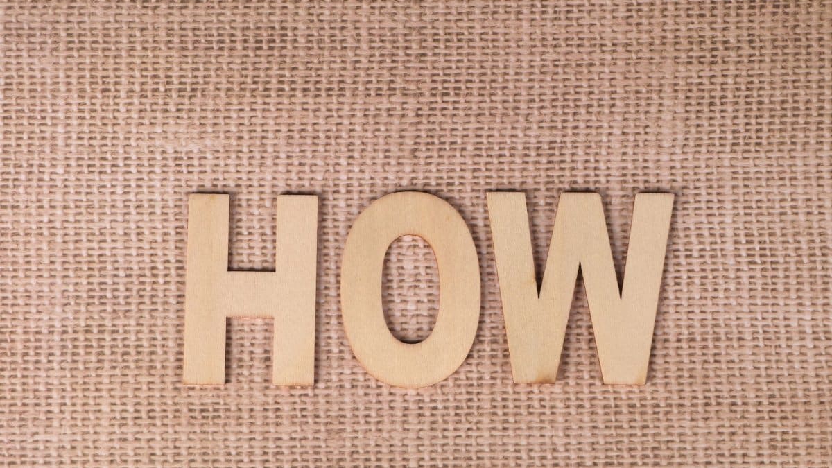 Word 'HOW' formed with wooden letters on textured burlap surface.